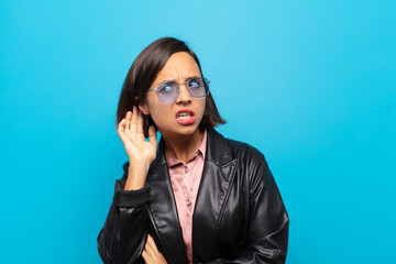 young hispanic woman looking serious and curious, listening, trying to hear a secret conversation...