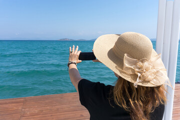 Woman tourist making a photo with her smartphone of the blue sky and water during a holiday vacation. Wearing a hat. Bodrum, Turkey, Aegean Mediterranean Sea