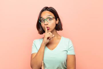 young hispanic woman looking serious and cross with finger pressed to lips demanding silence or...