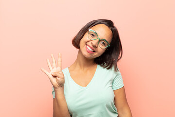 young hispanic woman smiling and looking friendly, showing number four or fourth with hand forward,...