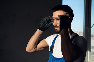 The worker is in a dark room. He puts on safety glasses