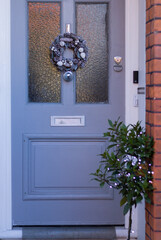 Merry Christmas is on threshold. Beautiful gray blue front door house with Christmas wreath decoration. English home style. Vertical image. 