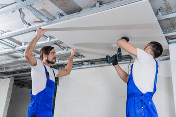 A team of adjusters are repairing the ceiling in an apartment. They are wearing blue work clothes