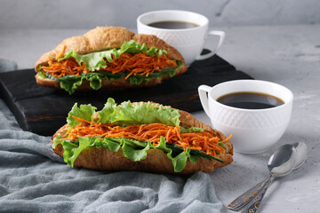 Vegetarian croissants-sandwiches with lettuce, carrots, cucumbers and two cups of coffee on a light grey concrete background. Breakfast or lunch concept
