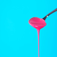 Pink fluid dripping from spoon on blue background 