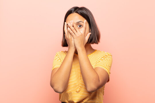 Young Hispanic Woman Feeling Scared Or Embarrassed, Peeking Or Spying With Eyes Half-covered With Hands