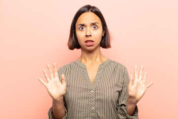 young hispanic woman feeling stupefied and scared, fearing something frightening, with hands open...