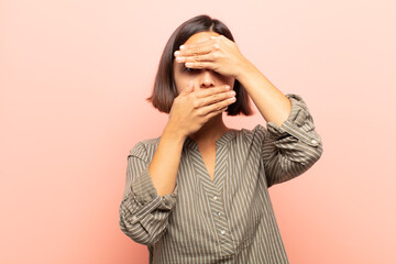 young hispanic woman covering face with both hands saying no to the camera! refusing pictures or...