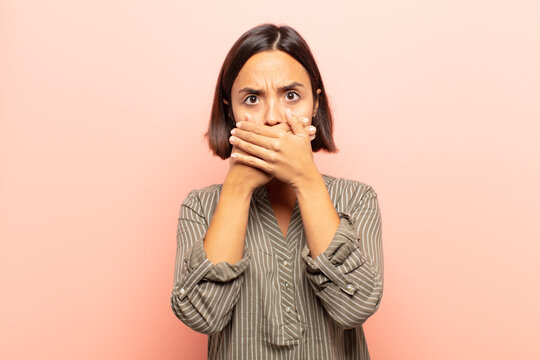 young hispanic woman covering mouth with hands with a shocked, surprised expression, keeping a secret or saying oops