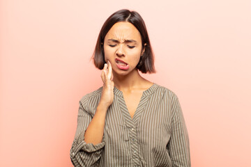 young hispanic woman holding cheek and suffering painful toothache, feeling ill, miserable and...