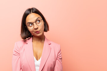 young hispanic woman with a worried, confused, clueless expression, looking up to copy space,...