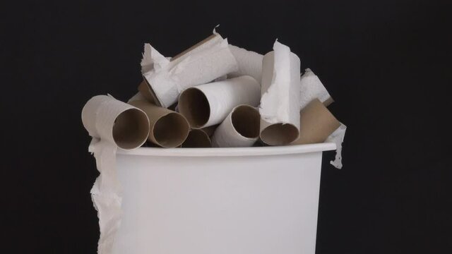 Used and empty rolls of toilet paper are shown in a small garbage bin, rotating slowly against a black background.