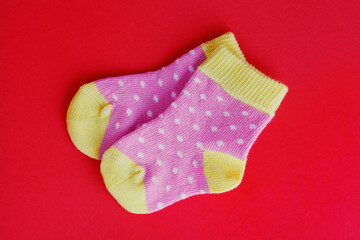 pair of funny colorful dotted pink and yellow baby socks on red background