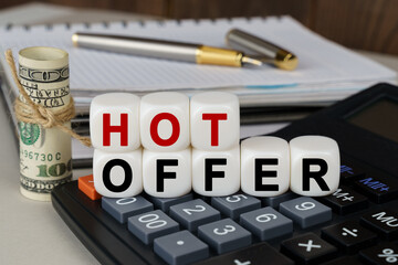 There are cubes on the calculator that say - HOT OFFER. Nearby out of focus - dollars, notebook and pen