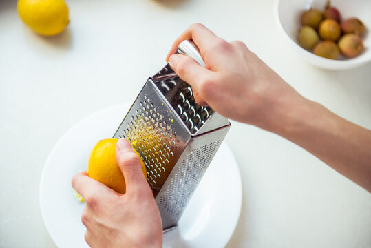 Top view male hands grating fresh whole lemon on metal hand grater, making zest on her kitchen table. Yellow and gray trendy colors of the year 2021. Selective focus. Copy space.