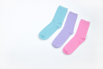 Multicolored children's socks without pattern, laid out in corner of frame, on white background with copy space, flatly, minimal style. Concept children's clothing, housekeeping