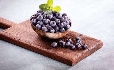 Bowl of fresh blueberries on rustic wooden board. Organic food blueberries and mint leaf for healthy lifestyle.