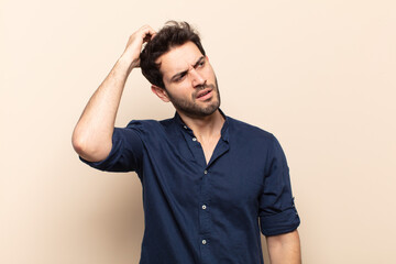 young handsome man feeling puzzled and confused, scratching head and looking to the side