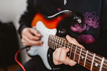 Young teenager boy hands playing electric guitar at home. Close up, selective focus.
