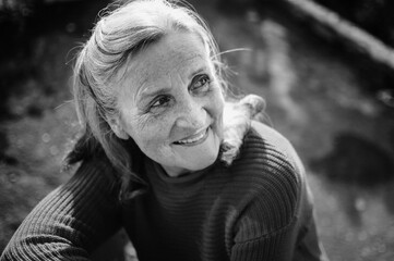 Black and white portrait of senior woman with grey hair and face with wrinkles outdoors relaxing at the park