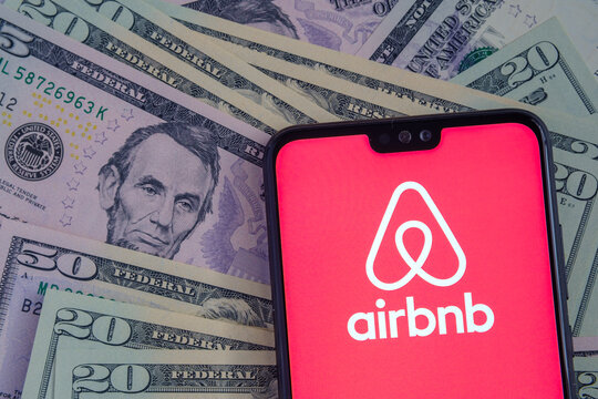 Stafford / United Kingdom - November 15 2020: Airbnb app logo seen on the screen of smartphone, placed on dollar bills.