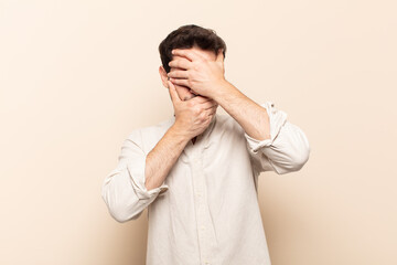 young handsome man covering face with both hands saying no to the camera! refusing pictures or...