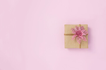 Present box made of kraft paper decorated with decorative poinsettia on pink background. DIY gift concept. Copy space