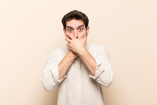 young handsome man covering mouth with hands with a shocked, surprised expression, keeping a secret or saying oops