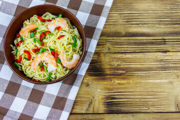 Bowl of instant Chinese noodles with shrimps, green onion and red hot chilli peppers on wooden table. Top view