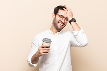 young handsome man laughing and slapping forehead like saying d’oh! I forgot or that was a stupid...
