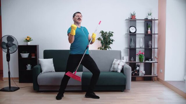 Young man janitor happily sings with a mop, posing as a rock star.