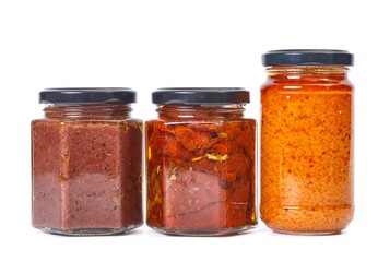 Jars pesto and dried tomato products on white background