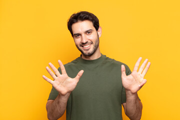 young handsome man smiling and looking friendly, showing number nine or ninth with hand forward,...