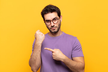young handsome man looking impatient and angry, pointing at watch, asking for punctuality, wants to...