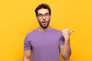 young handsome man looking astonished in disbelief, pointing at object on the side and saying wow,...
