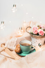 The atmosphere of a romantic morning, coffee in bed. Cup of coffee, profiteroles and gifts on a wooden tray on a silk bed. Home interior. Lifestyle