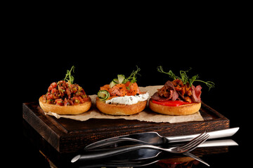 Assorted round bruschetta with various fillings (meat, vegetables, fish). Variety of small sandwiches. Delicious bruschetta. Three different flavors on one serving board