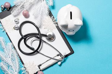 Creative flat lay overhead view of clipboard, medical stethoscope, piggy bank and festive Christmas...