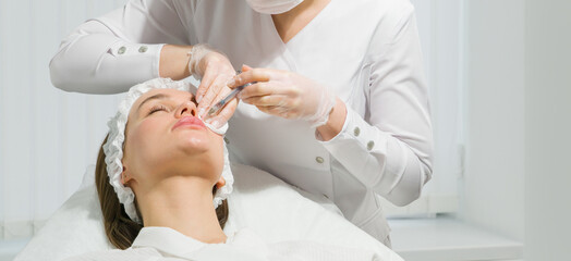 lip shape correction procedure in a cosmetology salon. The specialist makes an injection on the...
