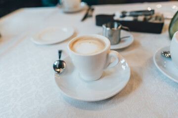 Small white cup of cappuccino stands on the table