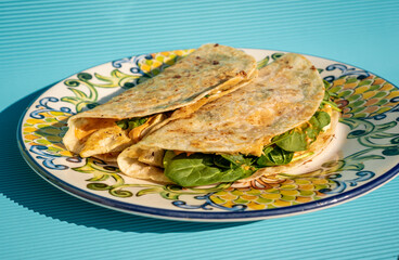 Delicious traditional quesadillas with chicken and spinach inside, on a handmade plate on a blue table.