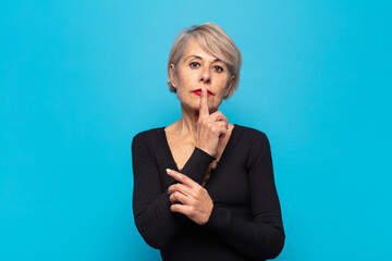 middle age woman looking serious and cross with finger pressed to lips demanding silence or quiet,...