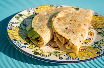 Delicious traditional quesadillas with chicken and spinach inside, on a handmade plate on a blue table.