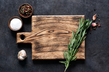 Cutting board with fresh rosemary and spices on a black concrete table. Top view with copy space