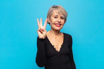 middle age woman smiling and looking friendly, showing number three or third with hand forward,...