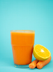 Exquisite orange juice with carrots inside a glass with carrots and half an orange on the side with a blue background.