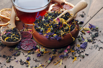 blended tea. black tea with dry flower petals and citrus fruits. dry black tea leaves in a wooden...