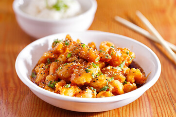 Asian honey glazed sesame chicken in a white bowl served with white rice; copy space