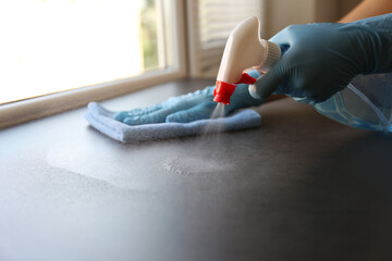 Woman in gloves cleaning grey window sill with rag and detergent indoors, closeup