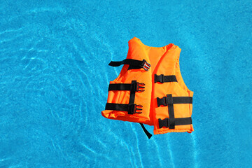 Bright orange life jacket floating in swimming pool, top view